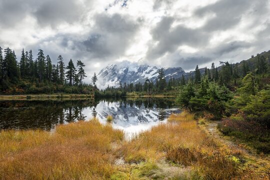 Mt. Shuksan in clouds, glacier with snow with reflection in Picture Lake, forested mountain landscape in autumn, Mt. Baker-Snoqualmie National Forest, Washington, USA