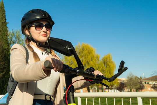 Woman riding electric scooter wearing helmet and sunglasses