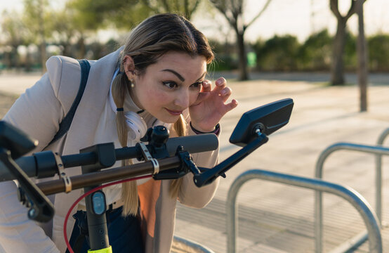 Woman adjusting her makeup in an electric scooter mirror