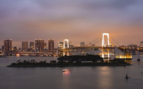 View of skyline with skyscrapers and illuminated Rainbow Bridge in the evening, Odaiba, Tokyo, Japan