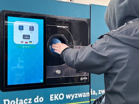 Person inserting a plastic bottle into a reverse vending machine for recycling in an urban environment in Gdynia, Poland April 20, 2026