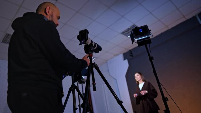 Man wearing black clothes stands near the camera. Low angle view. Woman in brown jacket talks to camera waving hands.