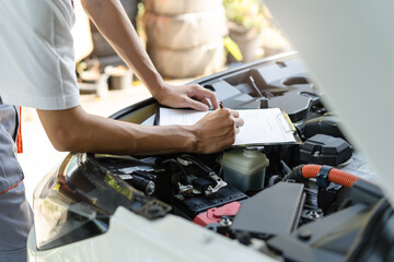 Naklejka premium Auto check up and car service shop concept. Mechanic writing job checklist to clipboard to estimate repair quotation to client at workshop garage.