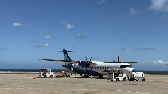 April 9th, 2026, Fuertaventura, Spain. Regional turboprop aircraft parked on apron with service vehicles under blue sky aviation travel scene