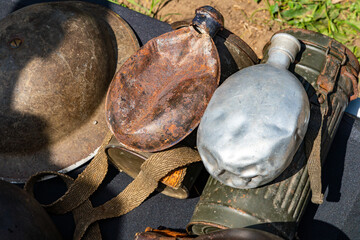 Obraz premium Collection of vintage military artifacts on a dark background: steel helmet, rusty canteen, dented aluminum flask, and a gas mask canister. Close-up view of historical war equipment and textures.