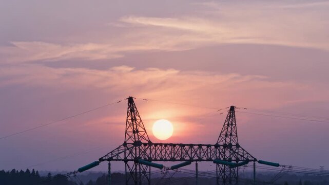 Rising sun moving through steel lattice towers at open utility corridor, exposing insulators