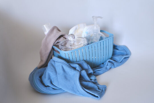 Blue basket filled with newborn hygiene products and clothes on white background