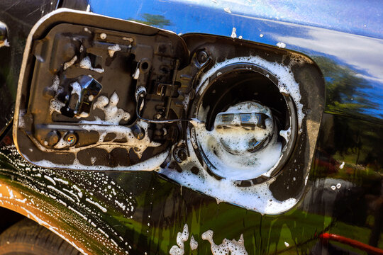 Service worker cleans fuel tank opening on vehicle with soap water while standing outside