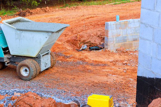 Construction vehicle moves concrete on building site with dirt unfinished wall sections.