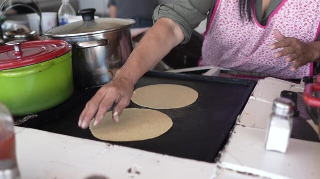 A woman prepares tacos at a taco stand in Baja California, Mexico, focusing on grilling tortillas and preparing fish fillings to serve.