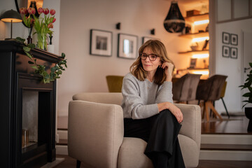 Obraz premium Blond haired attractive woman relaxing in an armchair in her modern apartment