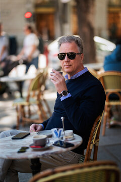 Confident mature man sitting at table at sidewalk cafe