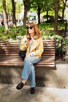 Confident blond haired woman with cellphone sitting a park bench and using her smartphone