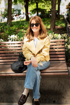 Confident blond haired woman sitting a park bench and enjoying a sunny day