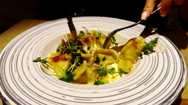 Cutting Ravioli With Knife And Fork On Elegant Ceramic Plate. Italian Dumplings With Creamy Sauce and Fresh Microgreens
