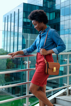 Vertical shot of young African American businesswoman leaning on office terrace railing, looking down thoughtfully. Ideal for corporate career growth, leadership, workplace branding