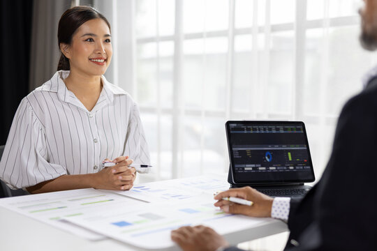 Professional Asian woman attending business meeting in office while attending a serious business meeting or job interview with a colleague using a tablet for data analysis.
