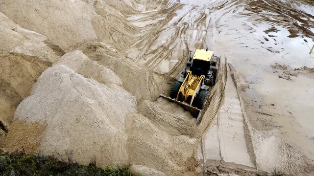 A large yellow tractor loader performs surface leveling on a sand quarry, loading and unloading of bulk materials from above with a drone. High quality 4k footage