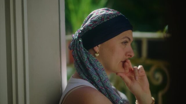 Mother undergoing chemotherapy close up on balcony with hand near face expressing contemplation, emotional strain, resilience and quiet reflection during difficult life moment