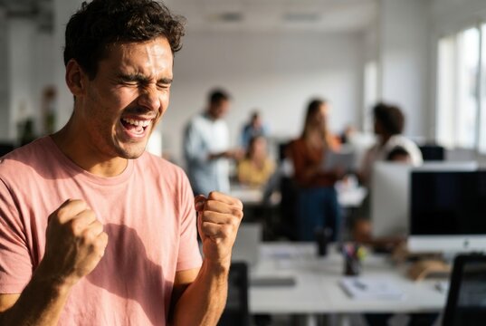 Young man celebrating achieving goals and winning with fists in a modern office