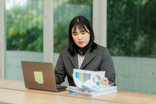 Young professional woman in an office, cross-referencing information from paper contracts with digital data on a screen, focusing on detailed vetting and accuracy.