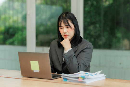 Young professional woman in an office, cross-referencing information from paper contracts with digital data on a screen, focusing on detailed vetting and accuracy.