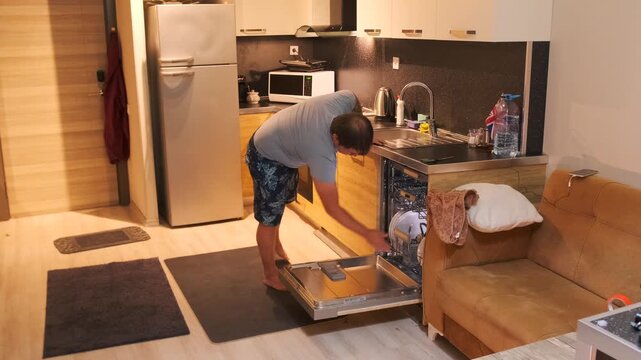 Man closing a dishwasher filled with dishes, sliding racks inside before starting cycle. Everyday kitchen routine, home cleaning, appliance use and domestic organization