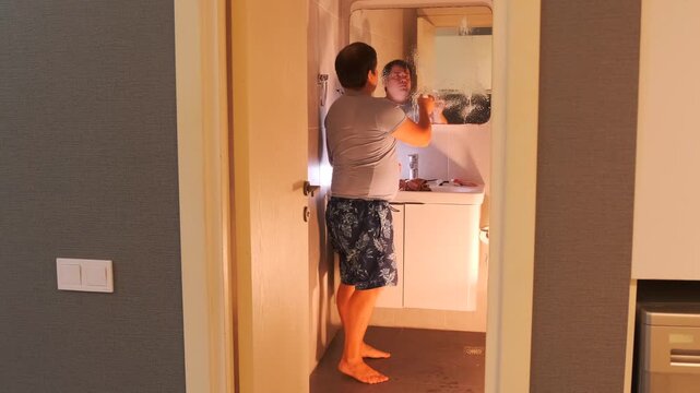 Man spraying cleaner and wiping bathroom mirror with cloth in home interior, household hygiene routine, removing stains and fingerprints from glass surface, everyday cleaning activity