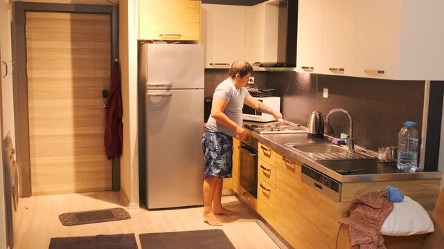 Man applying liquid cleaner from plastic bottle onto metal stove surface in kitchen, removing grease and dirt. Household cleaning routine, maintaining hygiene in a modern home interior