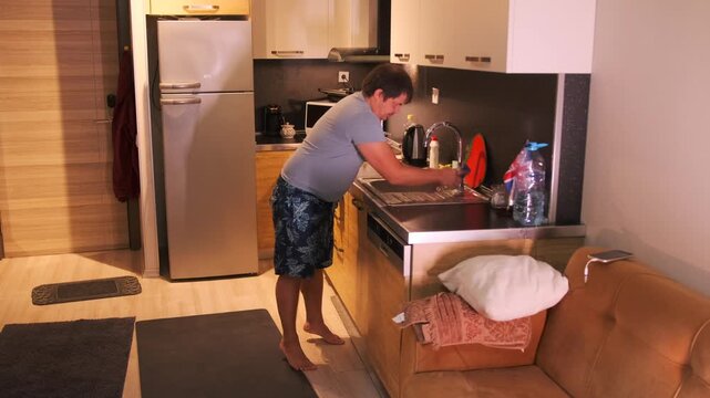 Man scrubbing kitchen faucet with brush to remove limescale and dirt, cleaning metal surface around sink, household hygiene routine, maintaining cleanliness in modern apartment kitchen interior