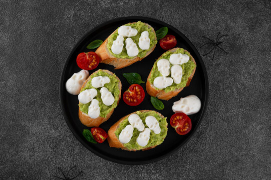 Halloween food. Avocado toasts with mozzarella in the shape of skulls and balsamic sauce on top. Funny food idea. Top view, copy space.