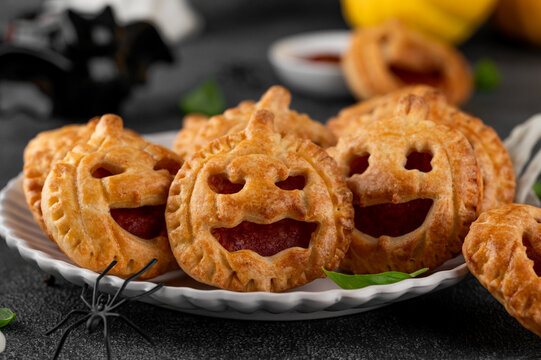 Halloween mini pies with tomato sauce, sausage and cheese. Jack-o-lantern pizza on plate on a dark background. Halloween food