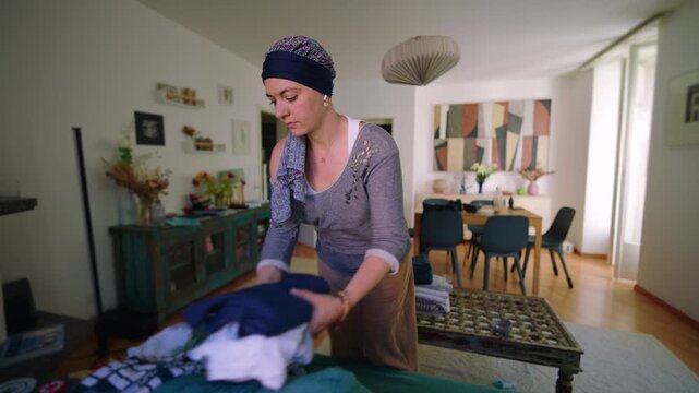 Woman undergoing chemotherapy folding clothes at home organizing daily domestic routine with calm focus expressing resilience, independence and continuity of everyday life 