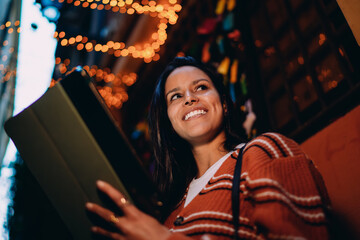 Young brunette woman rejoicing with tablet on night street, celebrating success, positive notification, winning opportunity, digital achievement, mobile banking, technology usage, authentic emotion. © BullRun