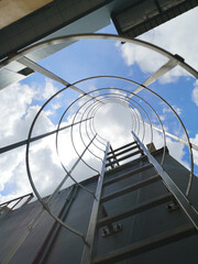 Stainless steel fixed ladder with safety cage viewed in strong perspective, symbolizing industrial access, maintenance, inspection, safety compliance, and risk prevention concepts © Stanley Fong