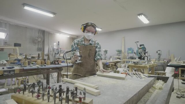 A skilled craftsman works in a woodworking workshop, utilizing power tools amidst various equipment and materials to create wooden items. The workspace showcases the art of woodworking in a vibrant, h