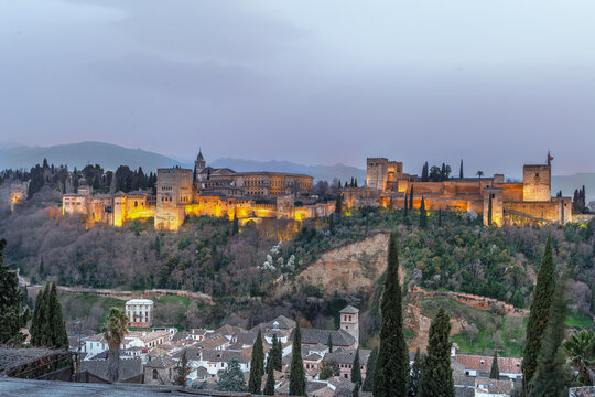 Illuminated Alhambra palace complex in Granada Spain at evening. Panoramic view from San Nicolas viewpoint under dusk sky