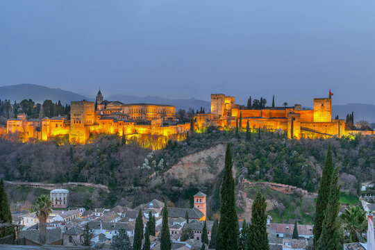 Illuminated Alhambra palace complex in Granada Spain at evening. Panoramic view from San Nicolas viewpoint under dusk sky