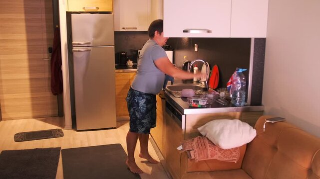 Man drying washed dishes with a towel and placing them into a kitchen cabinet. Everyday home routine, domestic cleaning, neat organization and kitchen hygiene
