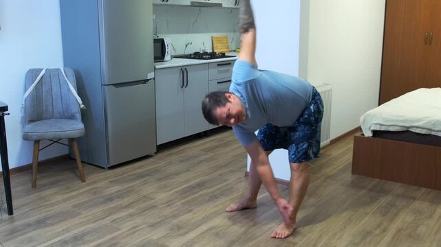 Man performs windmill exercise in home interior, stretching body and training flexibility with dynamic movement. Indoor fitness routine, mobility workout, balance, coordination and healthy lifestyle