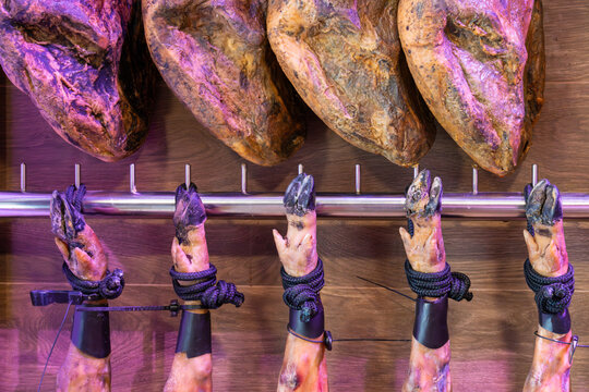 Traditional Spanish Jamon Iberico ham legs hanging in a deli shop. High-quality cured meat with black hooves (Pata Negra) displayed on a wooden wall in a gourmet restaurant
