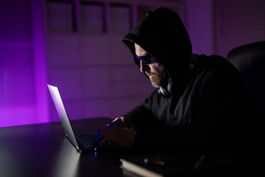 Hacker programmer in hoodie at office laptop, gaming. Hacker attack. Hacker gamer at night in office. Cyber attack. Cyber criminal and stolen financial data. Digital money thief. Code breaker