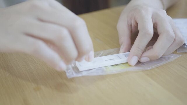 A close-up view of hands opening a health test kit on a wooden table, highlighting personal health management.