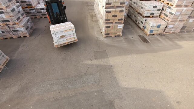 A forklift carries boxes through an open warehouse. Equipment transports goods through an open warehouse.