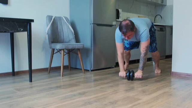 Man performs ab wheel rollout exercise on floor in home kitchen, training core muscles and balance. Indoor workout, fitness routine, strength training, healthy lifestyle and body control