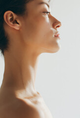 Fototapeta premium Side Profile Portrait of a Young Person with Short Dark Hair Looking Upwards with a Calm Expression Against a Clean White Minimalist Background