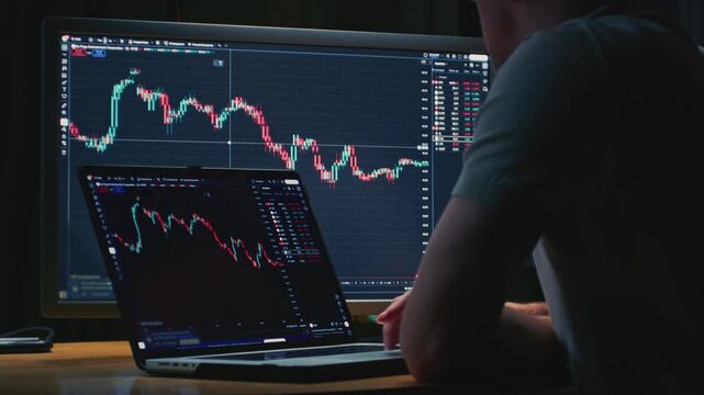 Man trader monitors market charts on laptop, screen and smartphone at home. Analyzing real-time trading data, considering investment strategies. Professional investor engaged in day trading, Evening