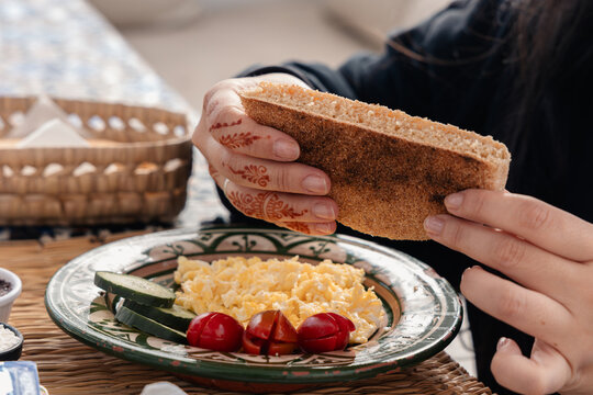 Womans hands with henna holding khobz bread during traditional Moroccan breakfast with scrambled eggs and fresh vegetables