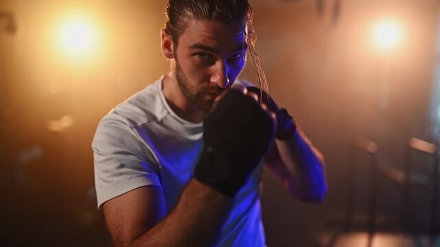 Determined muscular man shadowboxing in a moody gym with dramatic lighting. Fighter practicing his punching technique