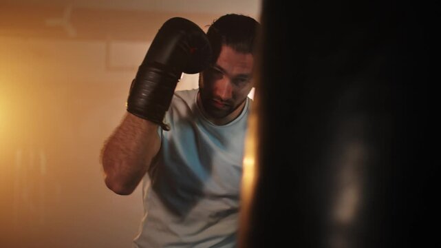 Determined male boxer hitting a punching bag during a workout session in a gritty, atmospheric gym with dramatic lighting